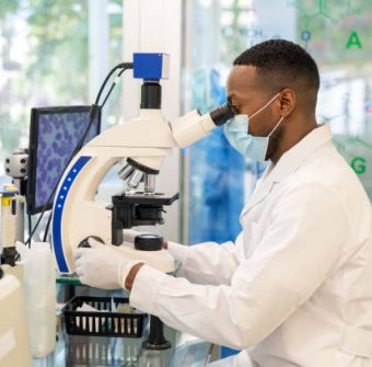 Side view of a medical researcher looking through a microscope. Male doctor wearing protective face mask using an electron microscope in a medical research center.