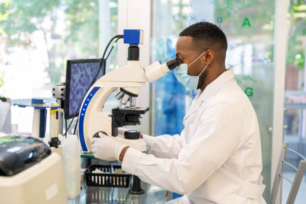 Lab Side view of a medical researcher looking through a microscope. Male doctor wearing protective face mask using an electron microscope in a medical research center.